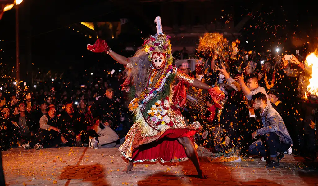 A masked Newar dancer performs a traditional cultural dance in Patan, Nepal, surrounded by a crowd during a night festival.