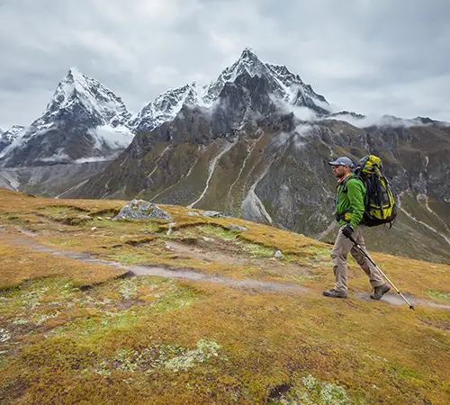 Trekker walking along an open trail near Dingboche, carrying a backpack and trekking poles with sharp snow-covered Himalayan peaks ahead.