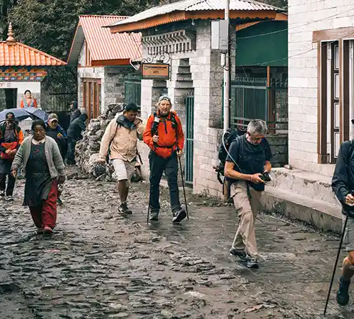 Trekkers walking through the stone-paved streets of Lukla village with backpacks and trekking poles after arriving in the Everest region.