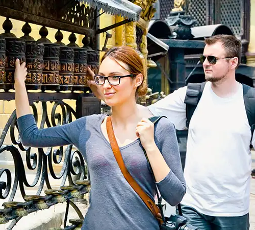 Tourists visiting a historic Buddhist site in Nepal, spinning prayer wheels while exploring local culture during their journey.