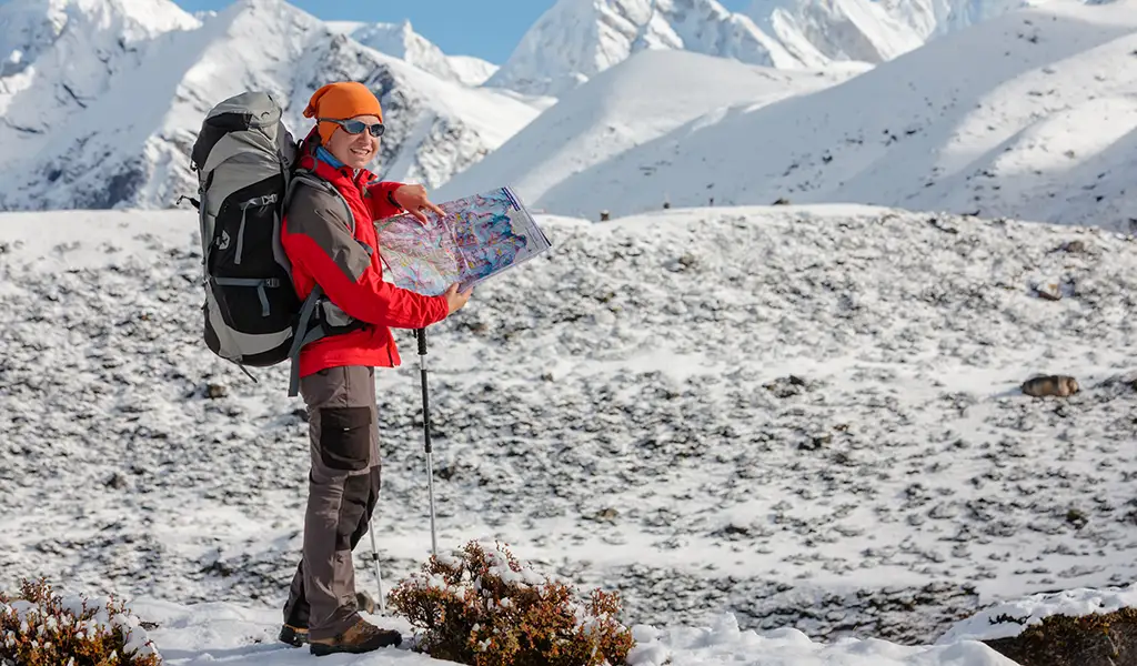 Trekker checking a map during the Annapurna Base Camp trek itinerary in snowy Himalayan mountains.
