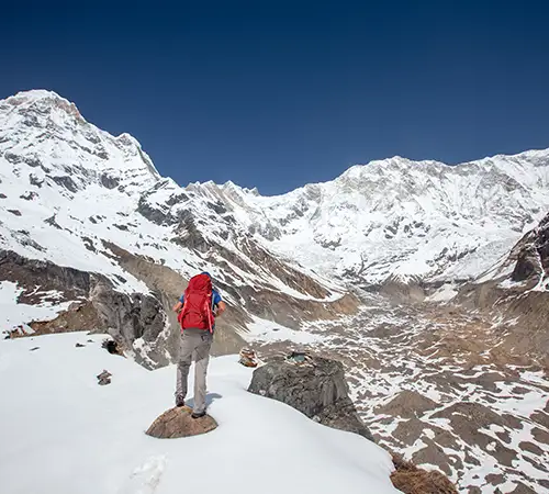 Trekker standing on a snowy ridge during the Annapurna Circuit trek, overlooking a wide valley surrounded by snow-covered Himalayan peaks.