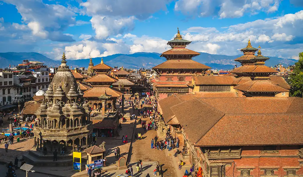A panoramic view of Patan Durbar Square in Lalitpur, Nepal, showing historic temples, traditional Newar architecture, and visitors in the courtyard.