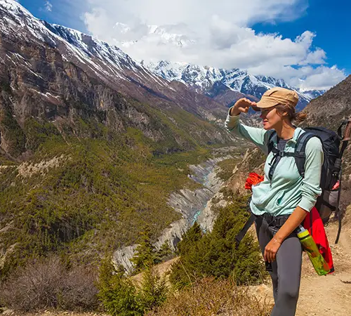 A trekker standing on a mountain trail overlooking a deep Himalayan valley and snow-capped peaks, reflecting on the everest base camp distance ahead.