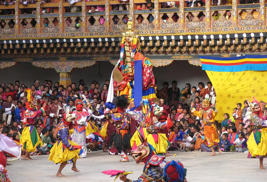 Monks and masked dancers perform a sacred ceremony during a Bhutan spiritual tour at a crowded festival.