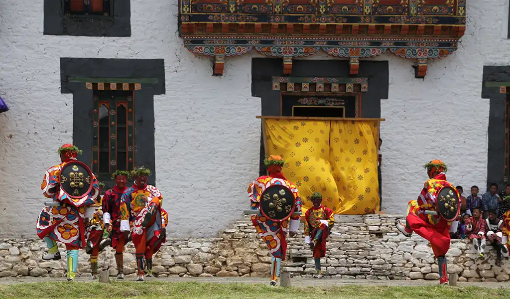 A masked dancer in traditional blue robes performs a sacred Cham ritual during a Bhutan spiritual tour festival.