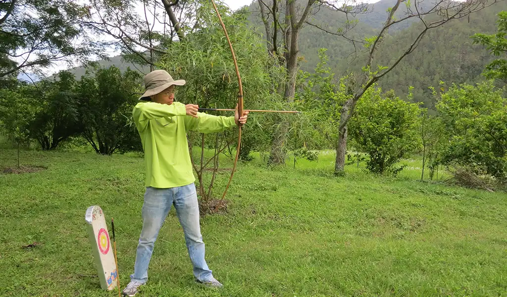 A young boy focuses as he aims a traditional bamboo bow during an archery lesson on a Bhutan family travel trip.