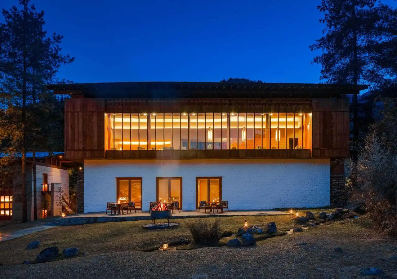 Luxury lodge in Bhutan surrounded by forest at night with warm interior lighting and outdoor firepit, ideal place for stay mentioned in Bhutan accommodation guide.