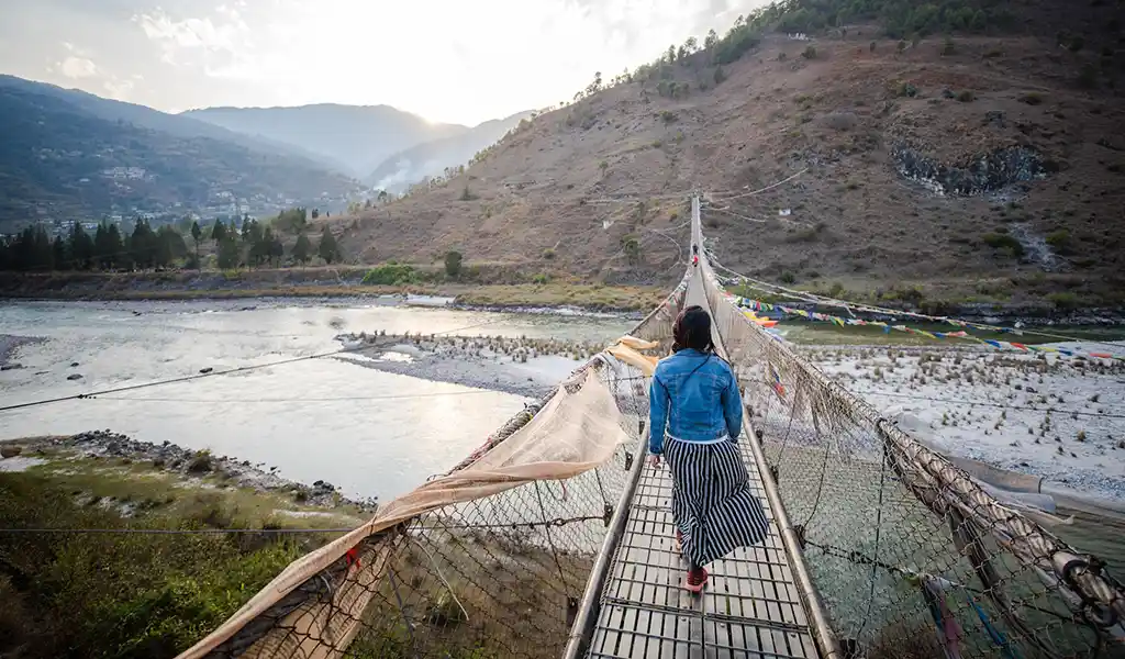 A happy traveler walking across the colorful Punakha Suspension Bridge, a must-visit spot for solo travel in Bhutan.