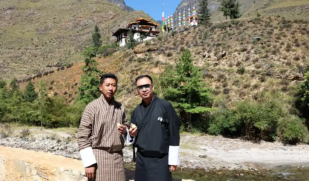 A happy solo traveler and their local guide sharing a conversation against the backdrop of a traditional Bhutanese temple.