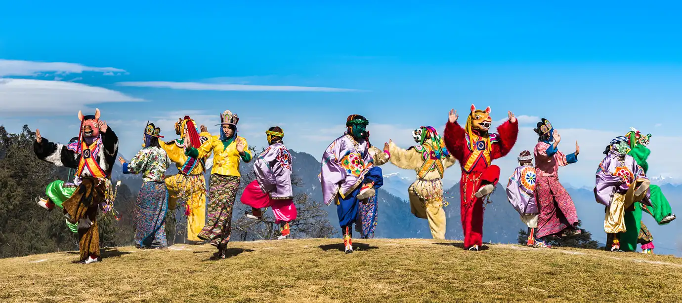 Traditional masked dancers performing at a Bhutan festival with Himalayan mountains in the background.