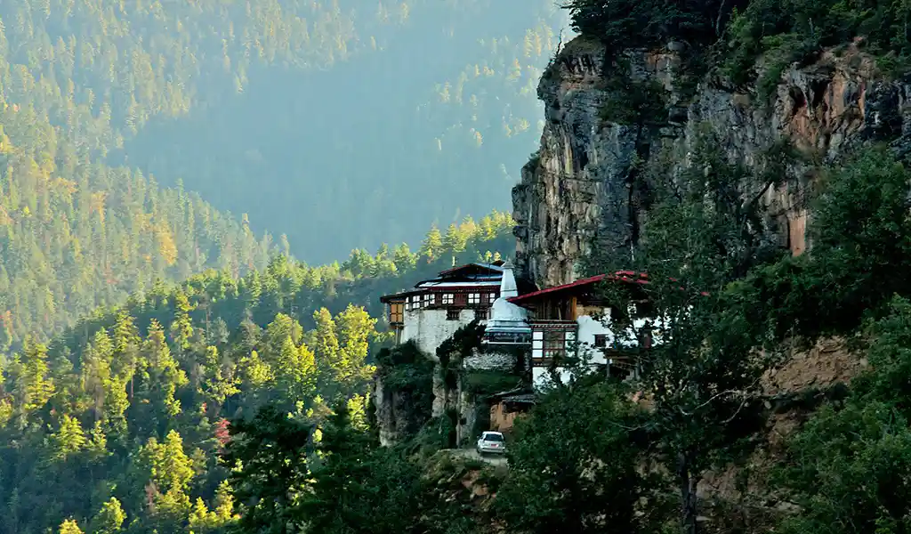 The Dzongdrakha Monastery, often called the mini Tiger's Nest Monastery, perched on a cliffside overlooking a lush forest in Bhutan.