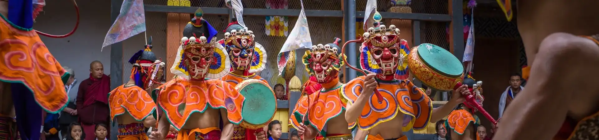Masked dancers perform drum cham dance at Jakar Festival in Bhutan wearing vibrant traditional costumes.