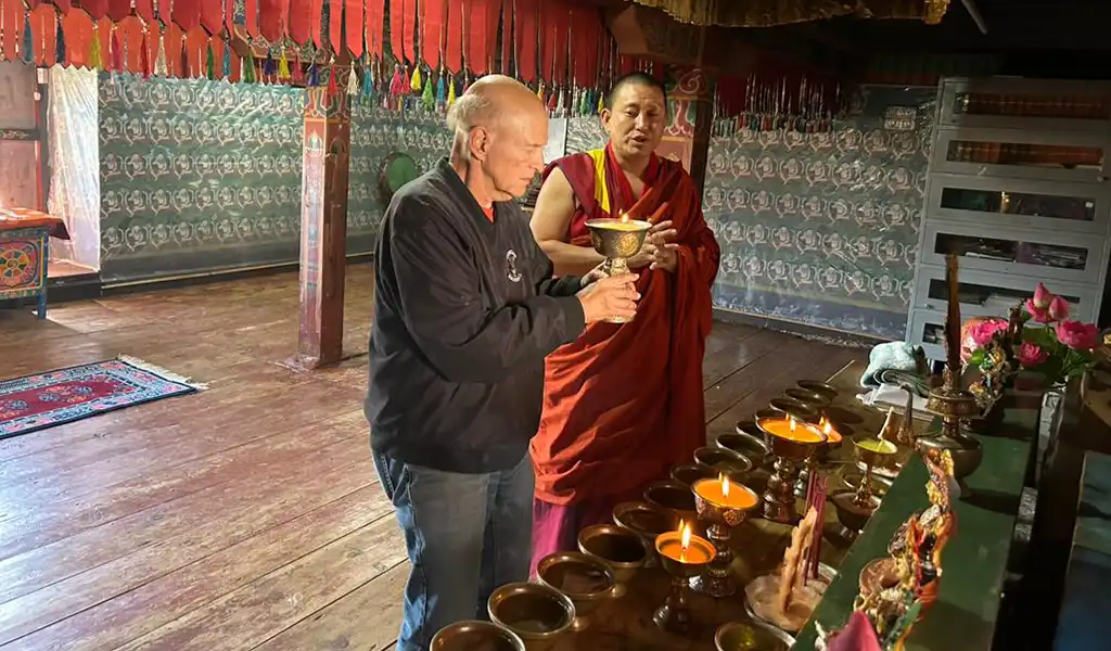Monk guiding a traveler during a butter lamp offering ceremony inside a monastery on a Bhutan Spiritual Tour.