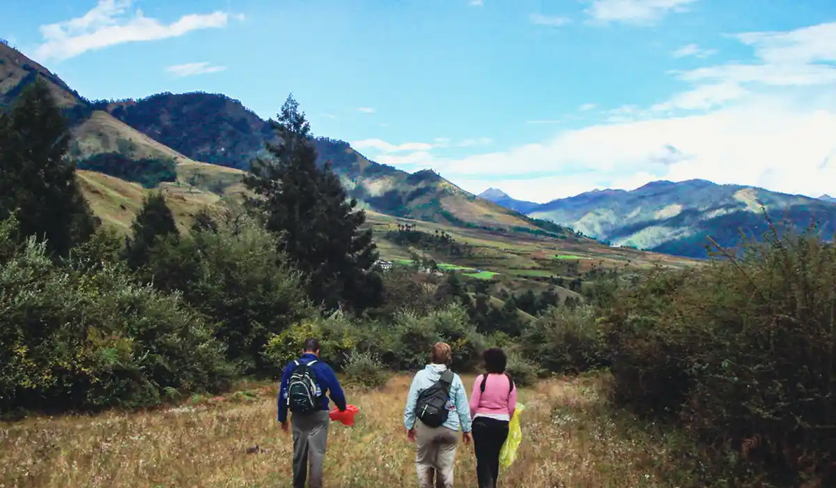 Hikers walking along Nabji Korphu Trail during Bhutan Off-Season Travel, surrounded by rolling hills, forests, and open valleys.