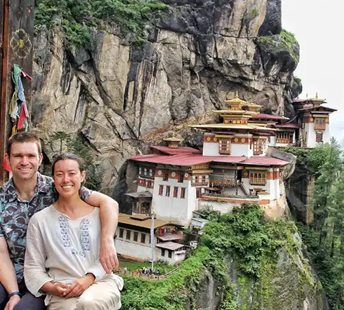 A happy couple smiling in front of the iconic Tiger’s Nest Monastery during a romantic Bhutan honeymoon tour.