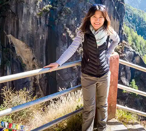 A traveler taking a photograph of the lush Paro Valley from a high-altitude viewpoint along the Tiger's Nest Monastery trail.