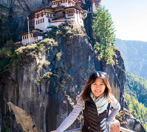 A close-up of a visitor taking a photo of the Tiger's Nest Monastery (Paro Taktsang) clinging to the cliffs above Paro Valley.
