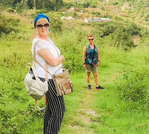 Two female travelers hiking on a narrow dirt path through lush green hills and terraced farmland during a Bhutan budget travel trip.