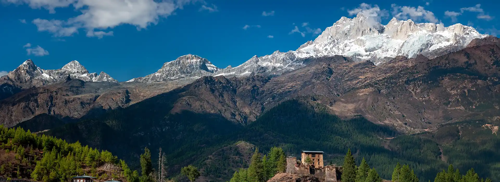 A panoramic view of snow-capped Himalayan peaks and a traditional stone fortress in a lush valley, perfect for a Bhutan travel guide.