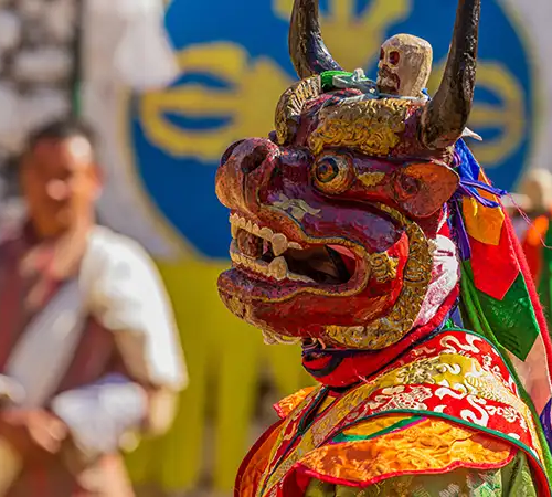 A masked dancer wearing a fierce red deity mask and ornate silk robes during a traditional festival on a Bhutan cultural tour.