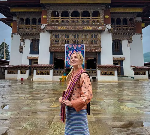 Female traveler in traditional Bhutanese dress standing in front of a historic dzong courtyard, featured in Bhutan travel FAQs.