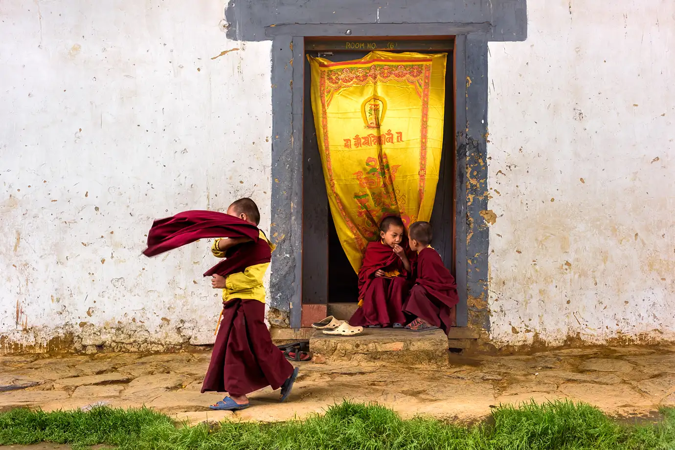 Young Buddhist monks playing and talking outside a monastery doorway in Bhutan.