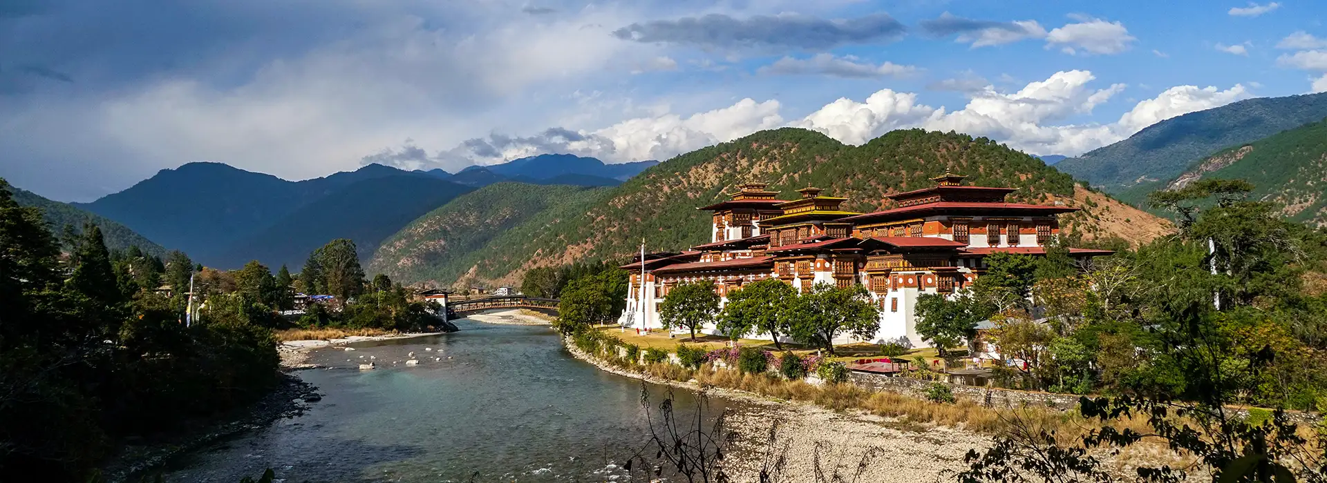 A wide panoramic view of the historic Punakha Dzong fortress in Bhutan, situated at the confluence of two rivers with lush green mountains in the background, illustrating a key destination accessible through the Bhutan Visa Process.