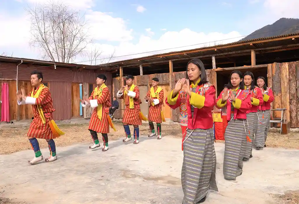 A group of Bhutanese youth performing a folk dance in traditional Gho and Kira attire during a Bhutan cultural tour.