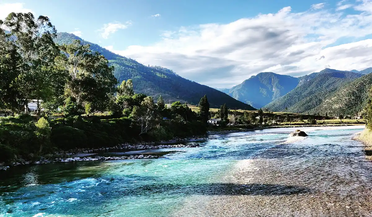Crystal-clear river winding through lush Himalayan valley in Bhutan during Bhutan Off-Season Travel, with forested hills and soft mountain light.