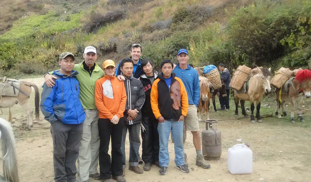 Hikers pause for a photo on the Druk Path Trek, with horses grazing nearby, featured in the Bhutan Wildlife and Nature Travel Guide.