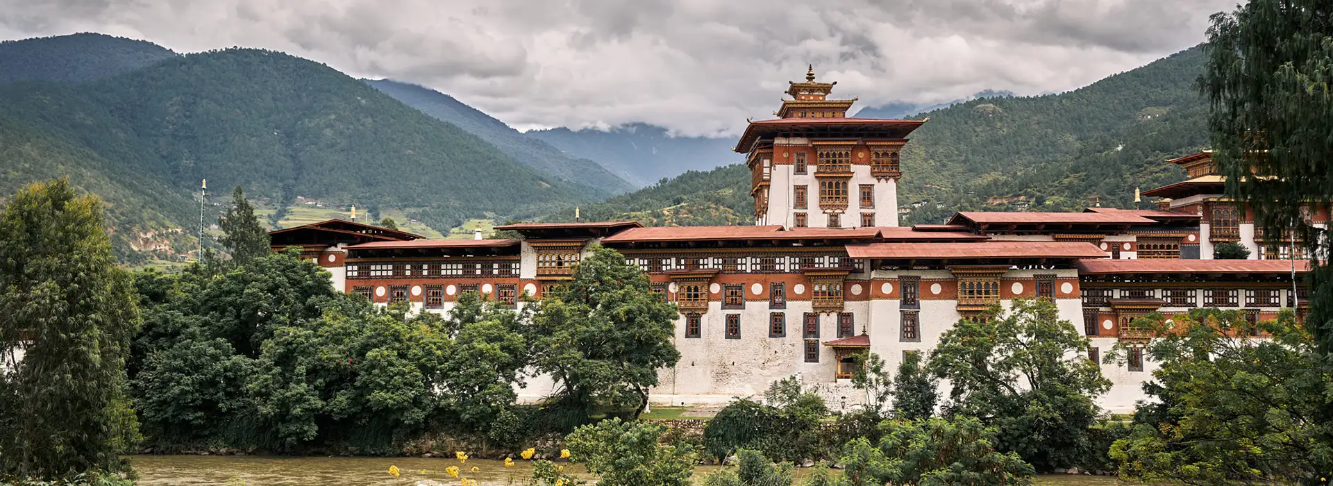Punakha Dzong standing beside a river surrounded by forested hills and mountains in Bhutan.