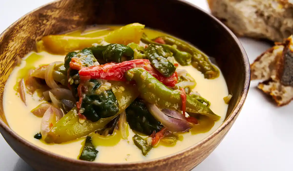 Traditional Ema Datshi with green chilies and melted cheese, representing Bhutan's Culture and Traditions in a rustic wooden bowl.