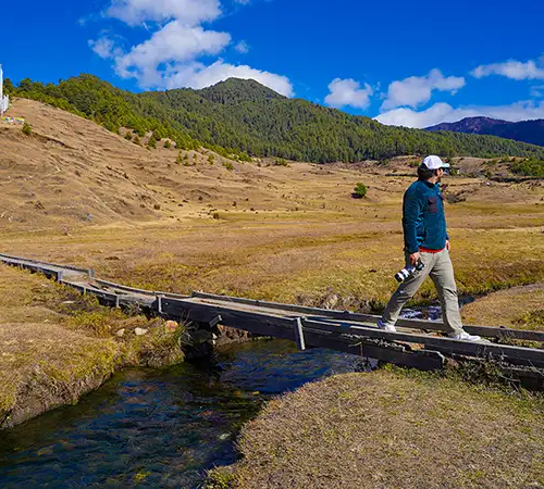 Traveler walking across valley in Gangtey under clear skies, showing Bhutan Weather in autumn season