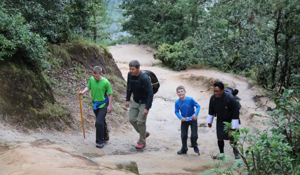 A family with young children hiking a scenic trail toward the cliffside Tiger’s Nest Monastery in Bhutan.