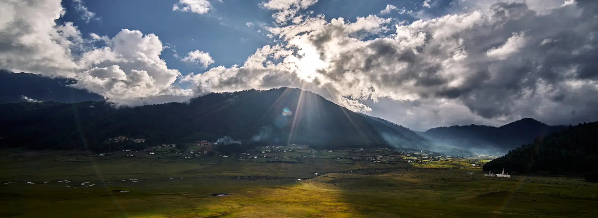 Sun rays illuminating the scenic landscape of Phobjikha Valley Bhutan with wide green plains and surrounding Himalayan mountains.