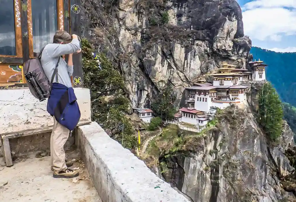 Traveler photographing Tiger’s Nest Monastery in Paro Bhutan, a popular highlight often mentioned in Bhutan travel tips.