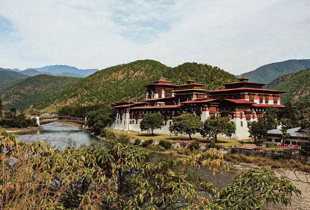 Punakha Dzong beside the Mo Chhu River, surrounded by green hills, showcasing Bhutan's Culture and Traditions in a scenic valley setting.