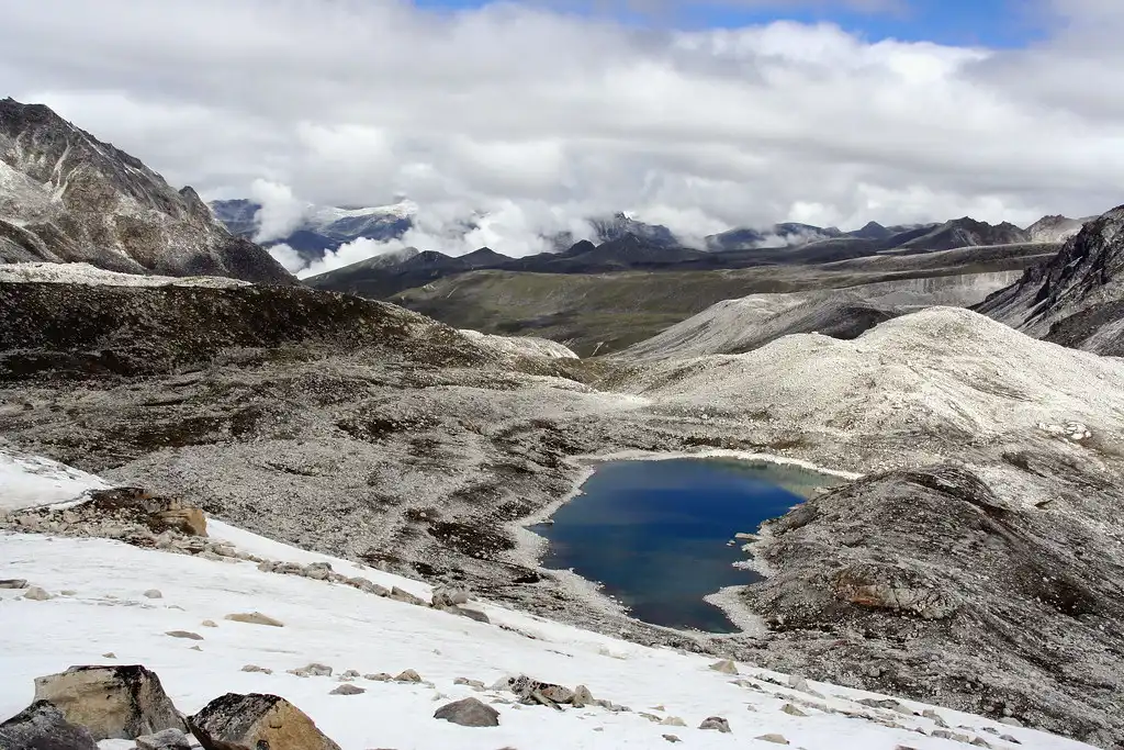 A deep blue glacial lake nestled among snow-covered rocky slopes and white moraine hills during a Druk path trek expedition in the Bhutanese Himalayas.
