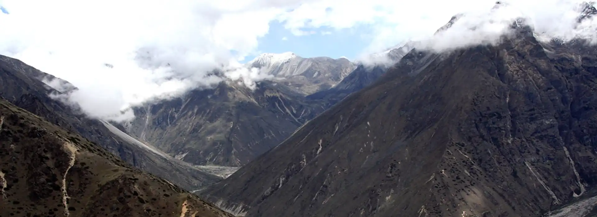 A panoramic view of deep mountain valleys and snow-dusted peaks under a cloudy sky during a Druk path trek or Snowman journey.