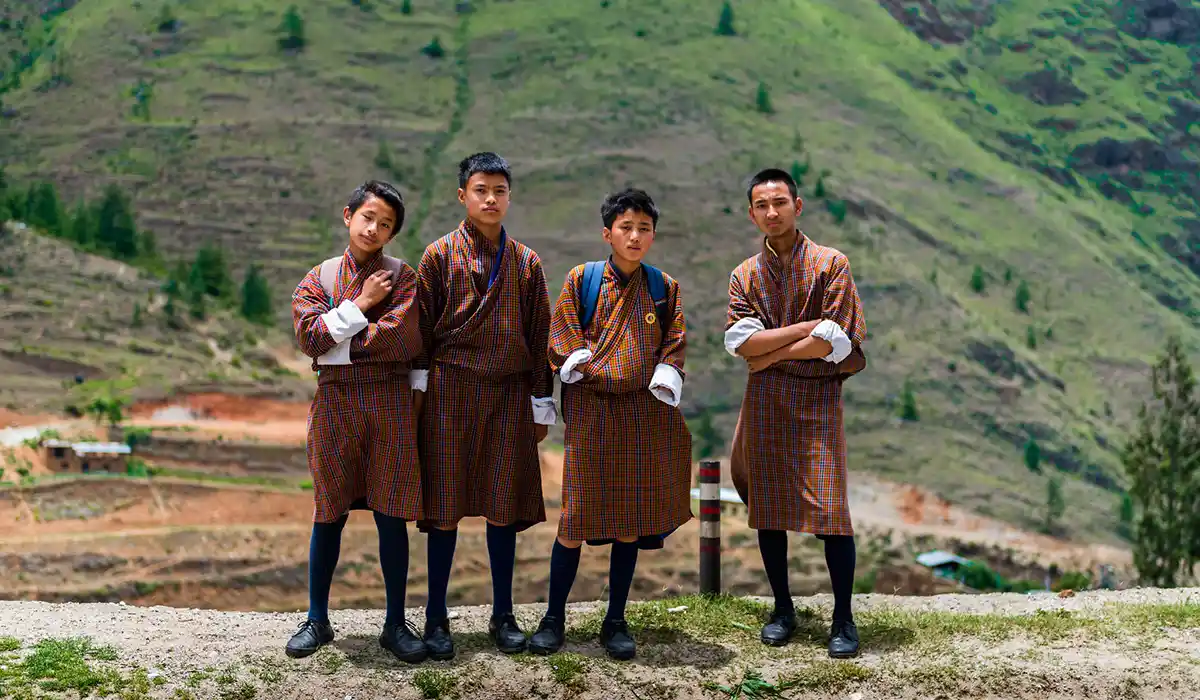 Young Bhutanese men wearing the traditional gho, reflecting Bhutan's Culture and Traditions against a scenic mountain landscape.