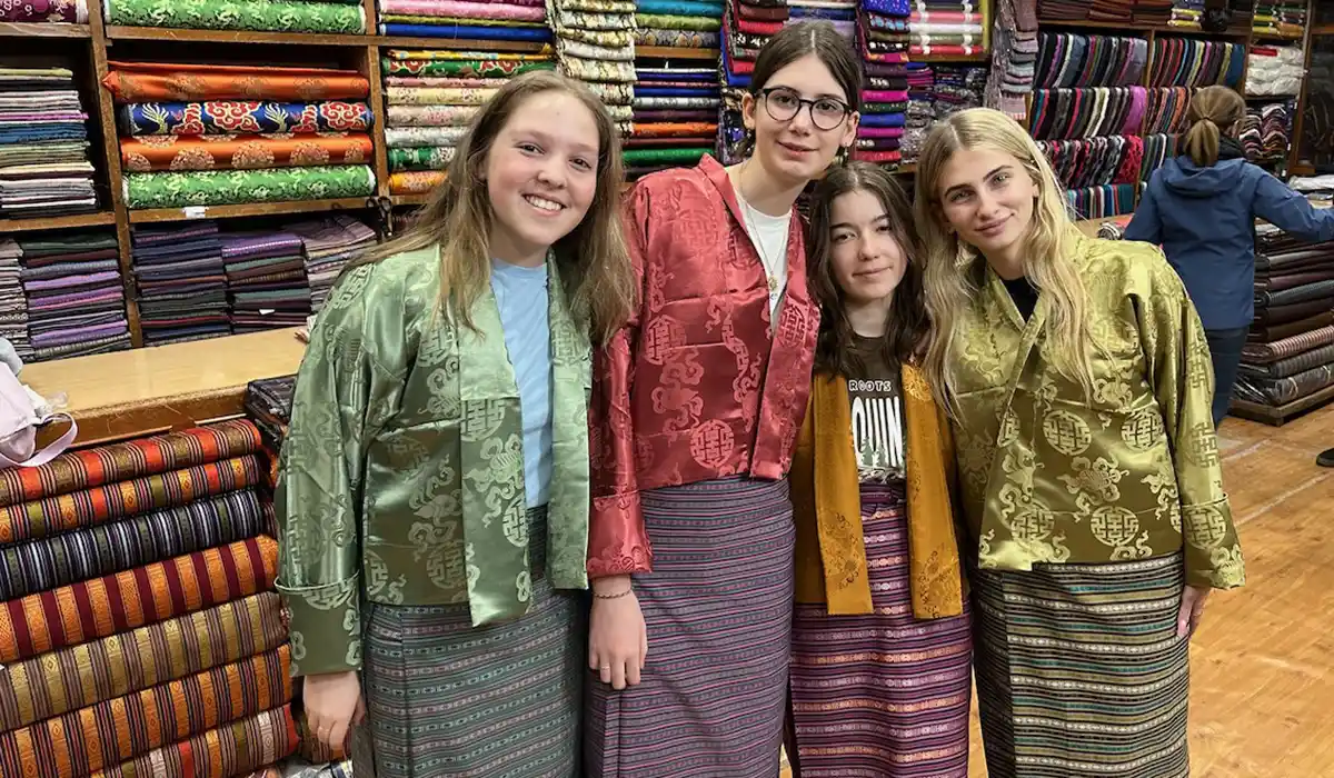 Young women wearing traditional kira in a Bhutan textile shop, reflecting Bhutan's Culture and Traditions through vibrant woven fabrics.