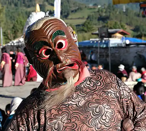 Masked festival performer in traditional attire at Bhutanese tshechu, reflecting Bhutan's Culture and Traditions in a vibrant outdoor setting.