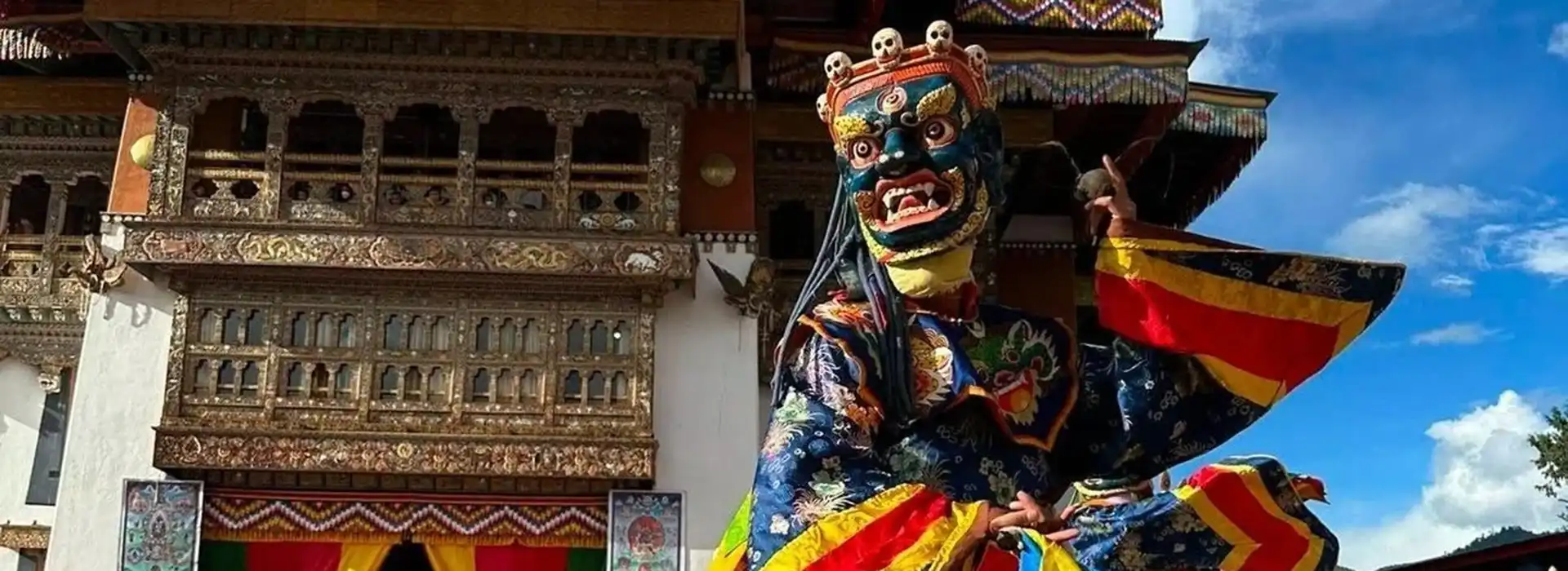 A masked Cham dancer in ornate blue robes performs at a temple during a Bhutan spiritual tour.