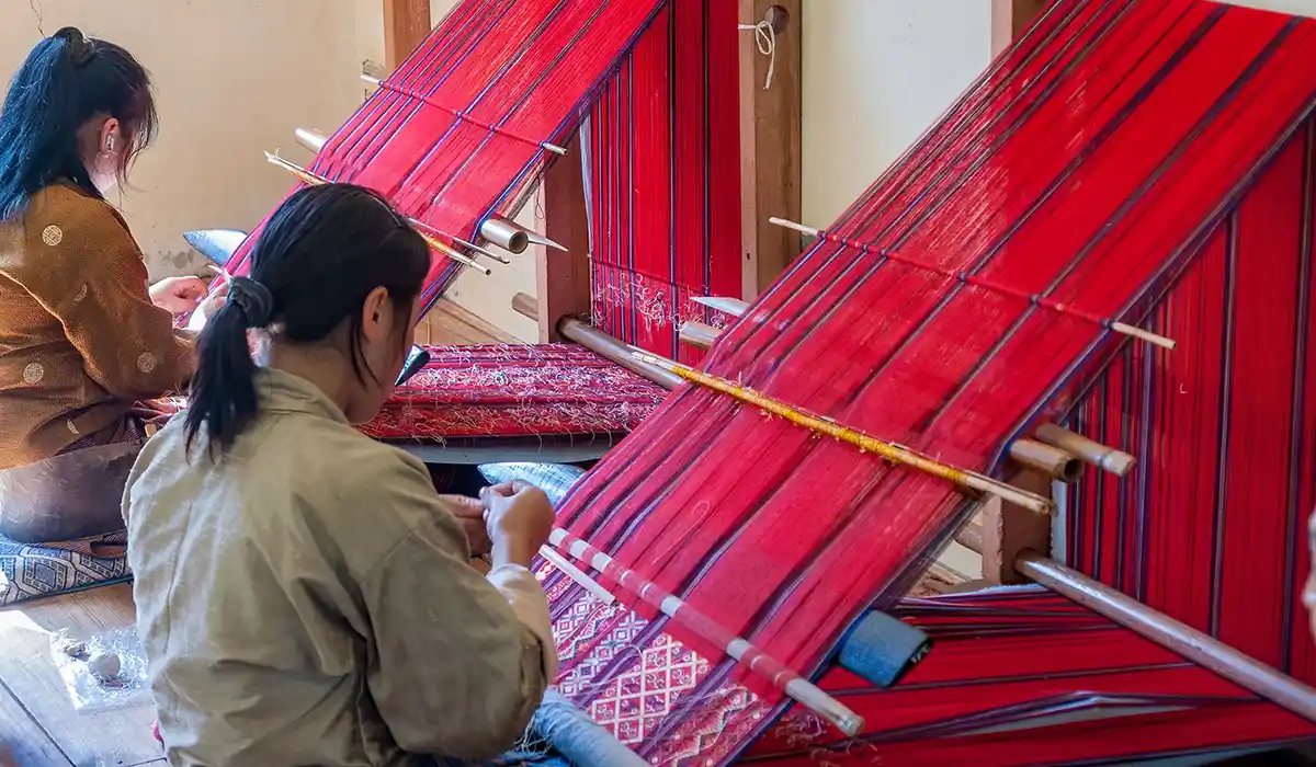 Bhutanese women weaving vibrant red textiles on traditional looms during Bhutan Off-Season Travel inside a local craft center workshop.