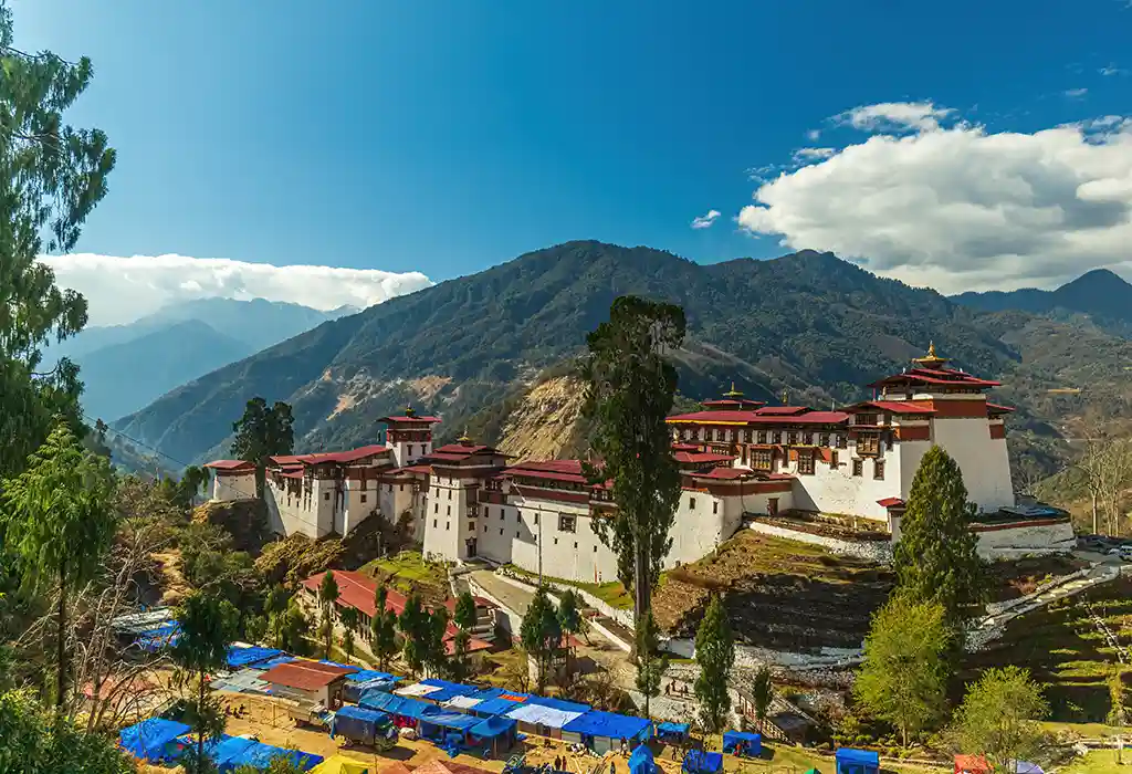 The massive white walls and red rooftops of Trongsa Dzong overlooking a mountain pass, one of the historic place to visit Bhutan.