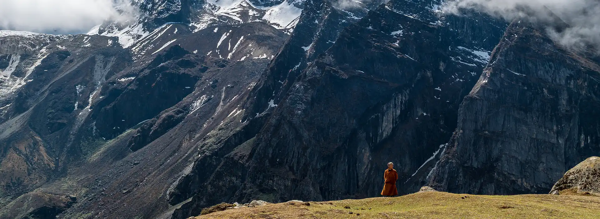 Monk standing before dramatic Himalayan cliffs, reflecting Eco-Friendly Travel in Bhutan and preserved mountain landscapes