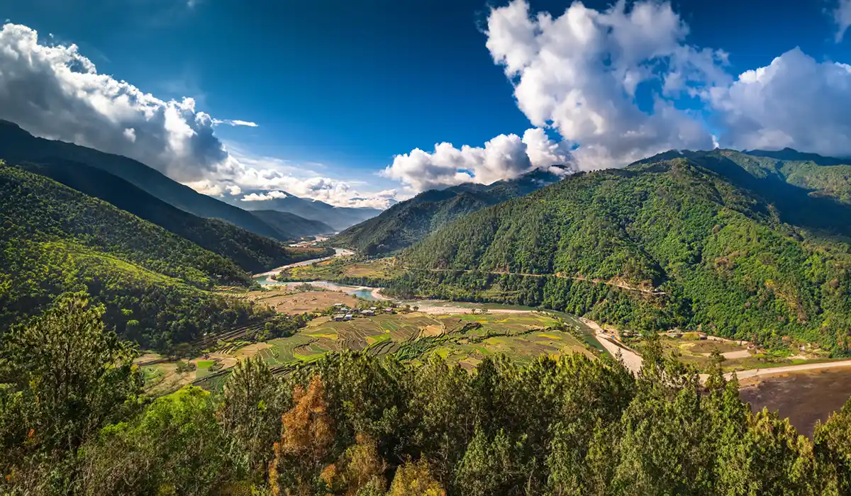 Panoramic Bhutan valley with winding river and terraced fields during Bhutan Off-Season Travel under dramatic clouds and lush green hills.