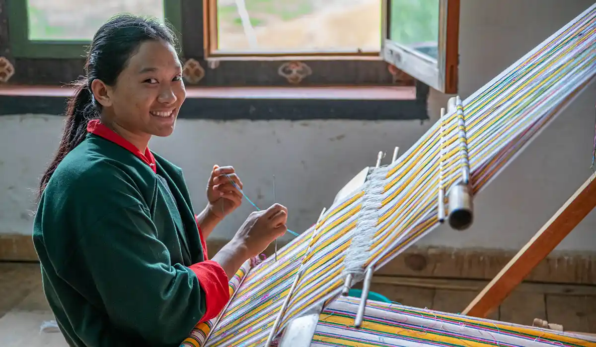 Bhutanese woman weaving colorful fabric on a traditional loom, preserving Bhutan's Culture and Traditions inside a bright workshop.