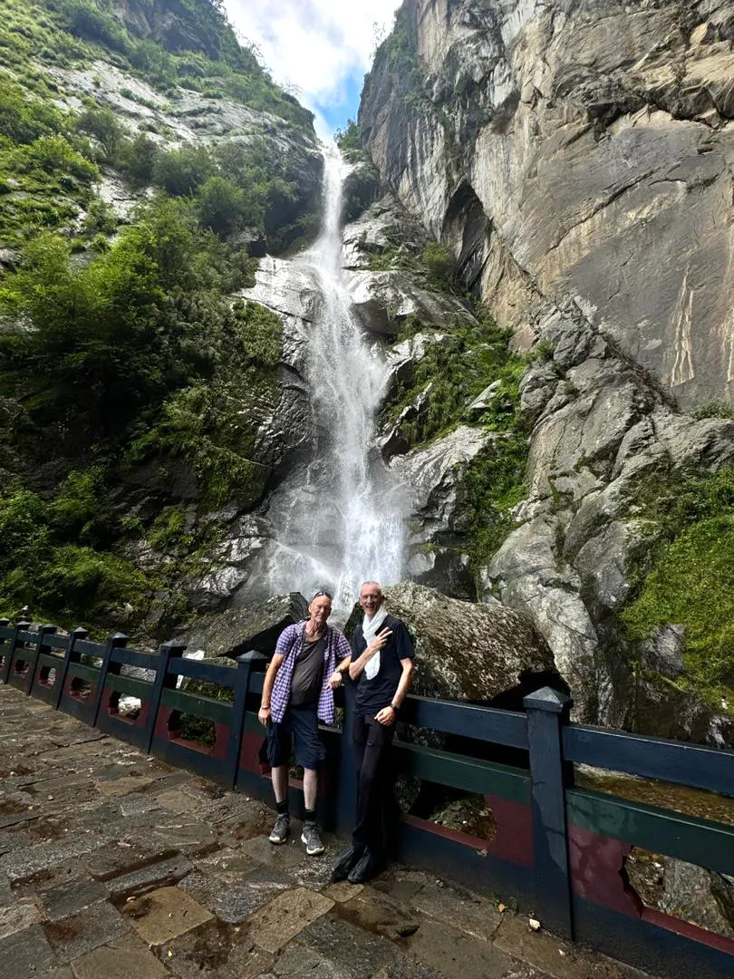 Travelers posing in front of a tall, cascading waterfall in the lush Bhutanese mountains, showcased in nature-focused Bhutan Tour Packages.